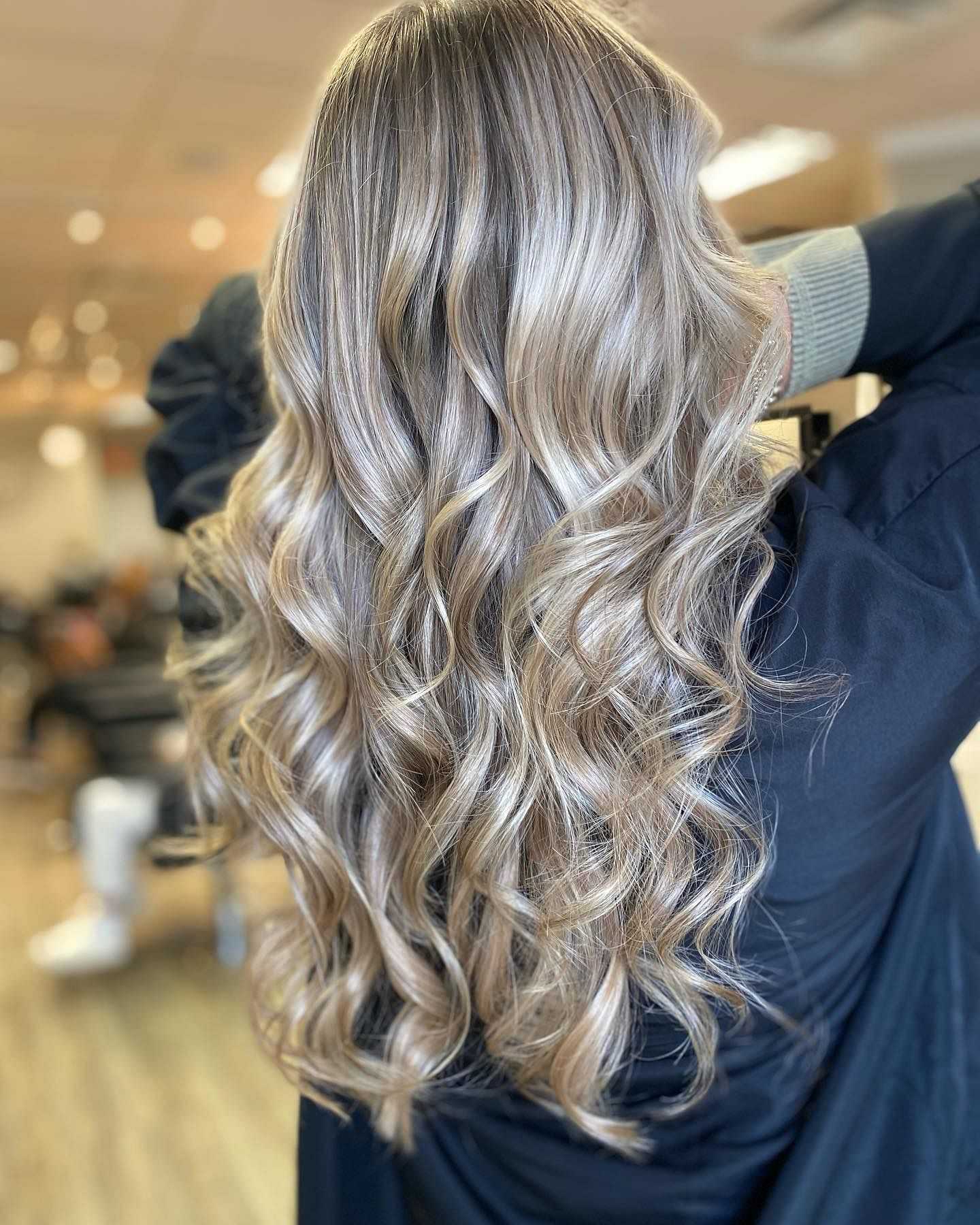 Woman with long, wavy blonde hair at a salon, showcasing freshly styled curls.